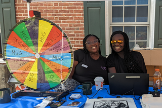 Two techs seated at a table with a colorful prize wheel