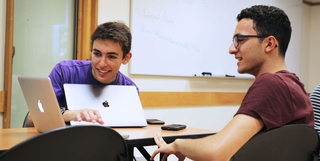 Two students looking at a laptop in a classroom with a whiteboard